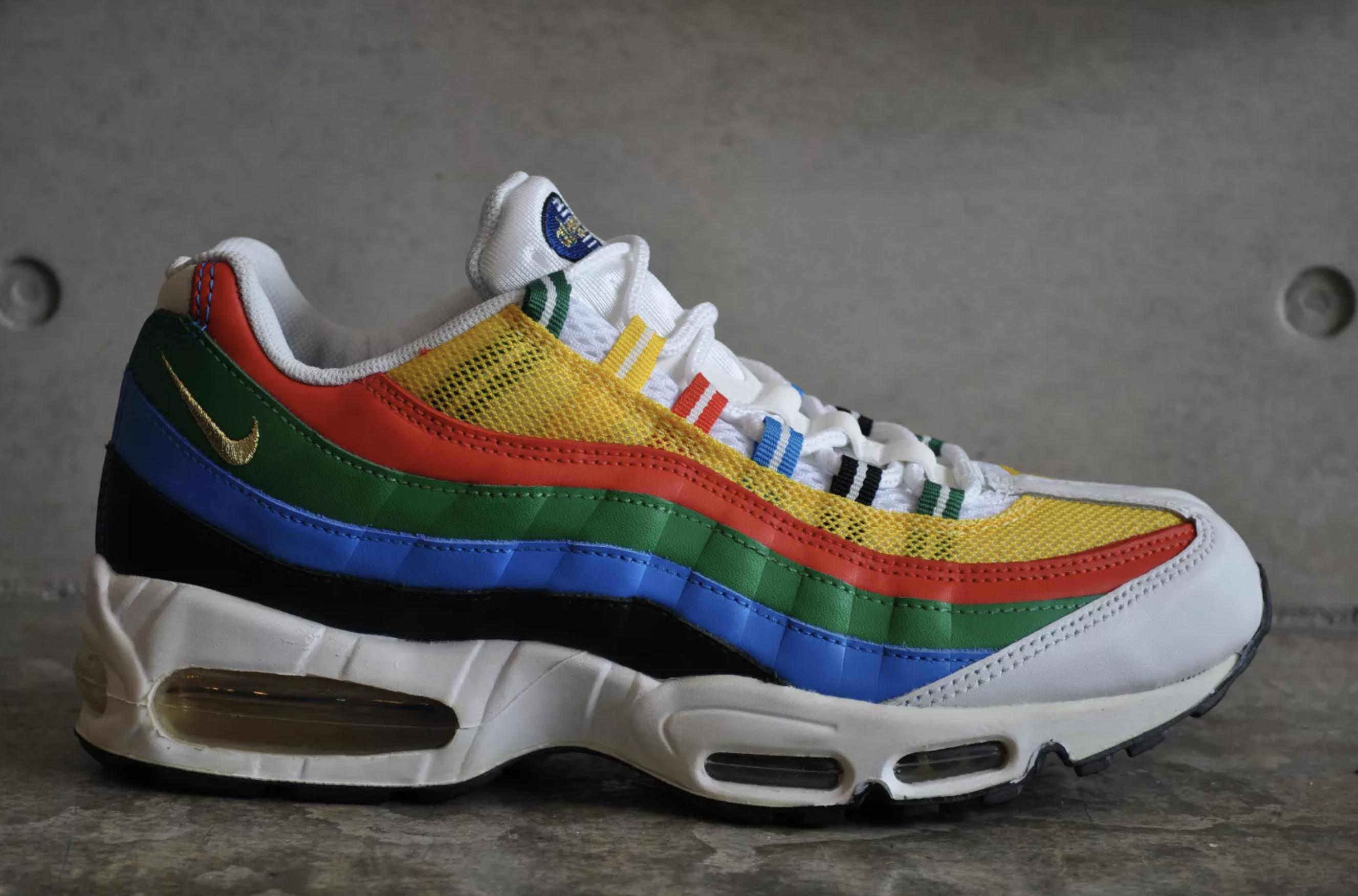 Nike Air Max 95 Olympic 2026 retro sneaker with multi-color Olympic ring-inspired design and gold Swoosh.