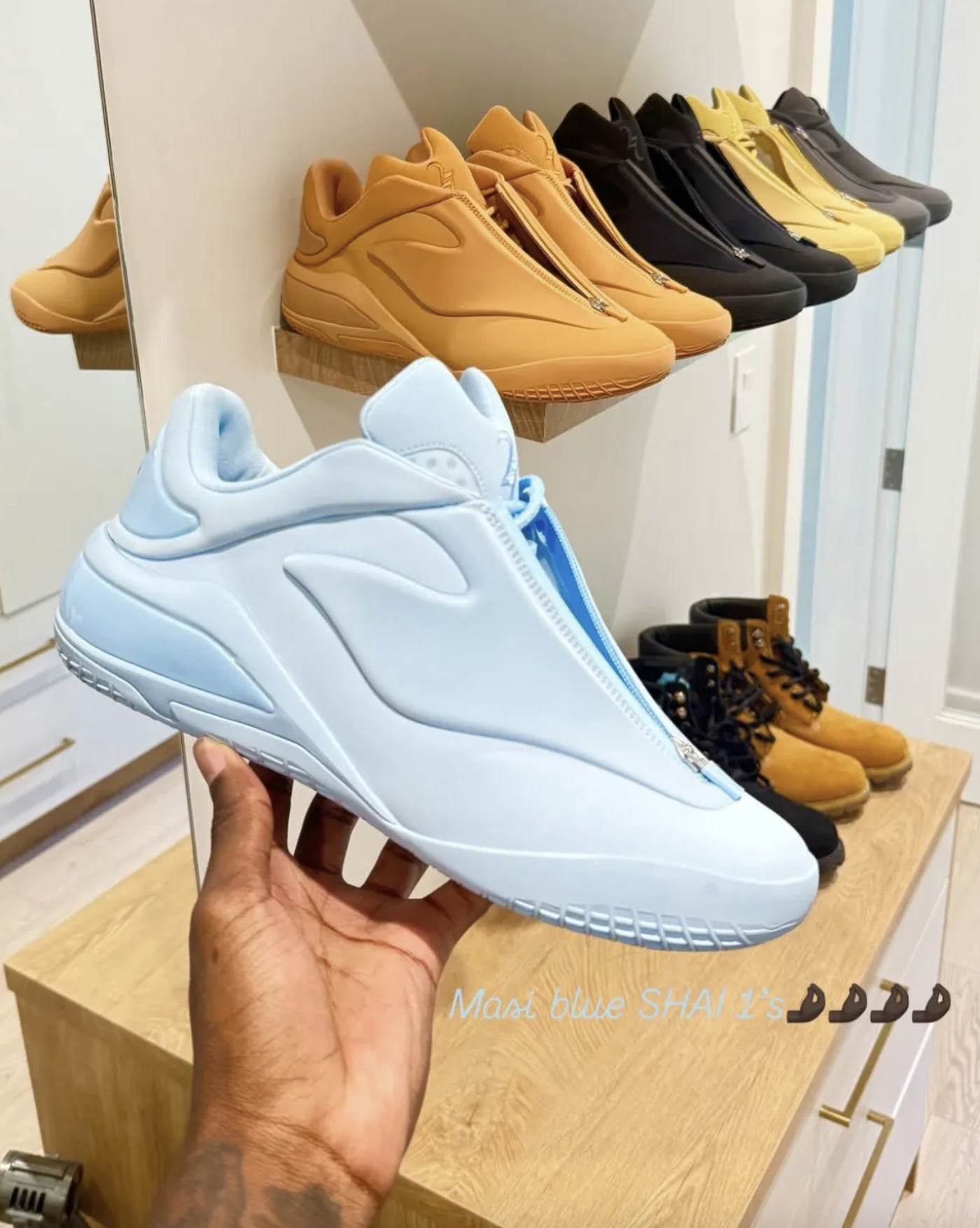 Close-up of Converse SHAI 001 “Masi Blue” held in hand, with multiple colorways on the background shelf.